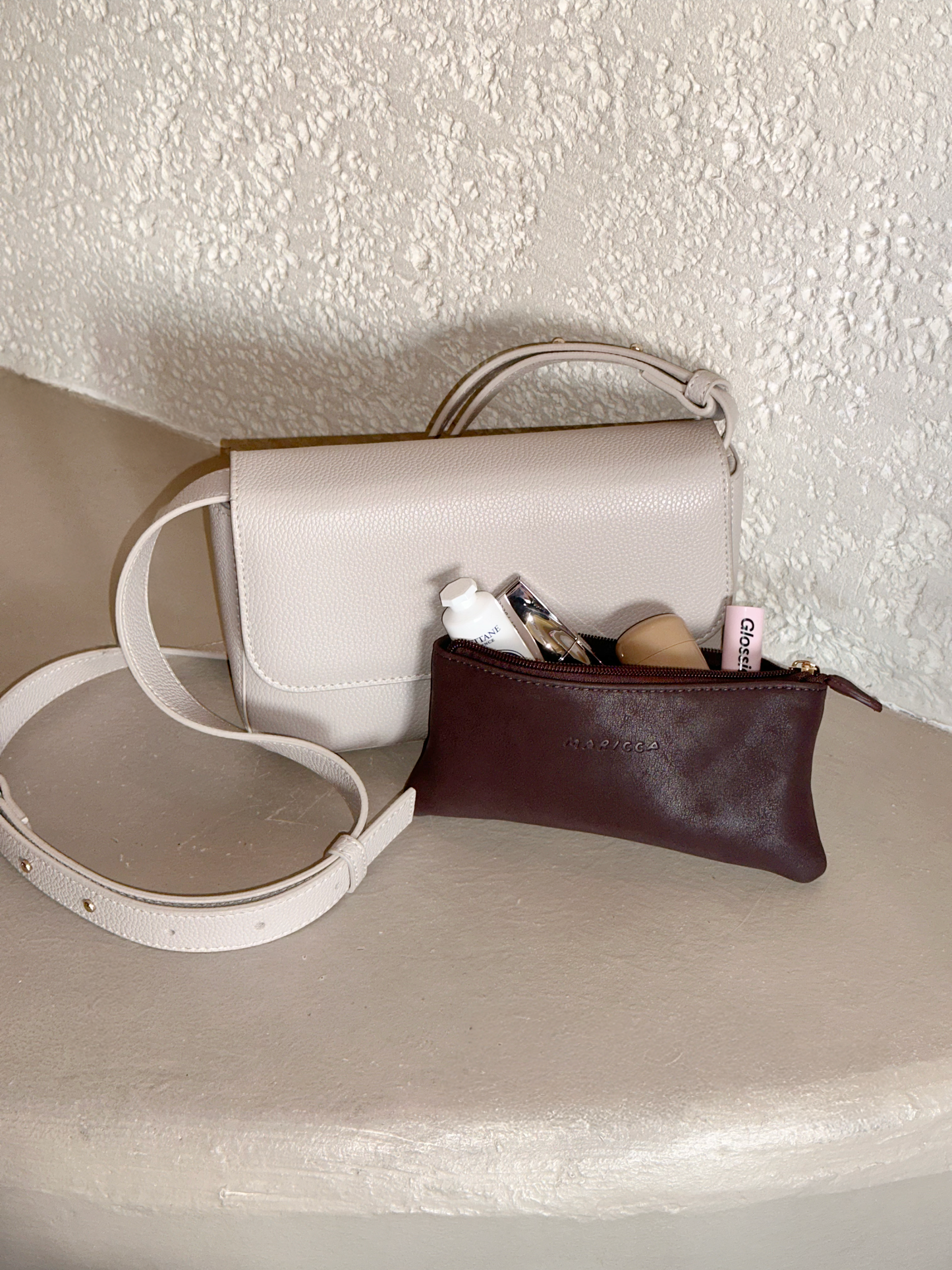 White handbag with the Cloud Pouch containing makeup items on a textured surface.